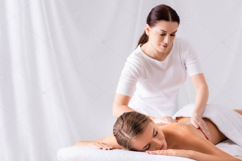 brunette masseur massaging back of woman on massage table in spa salon