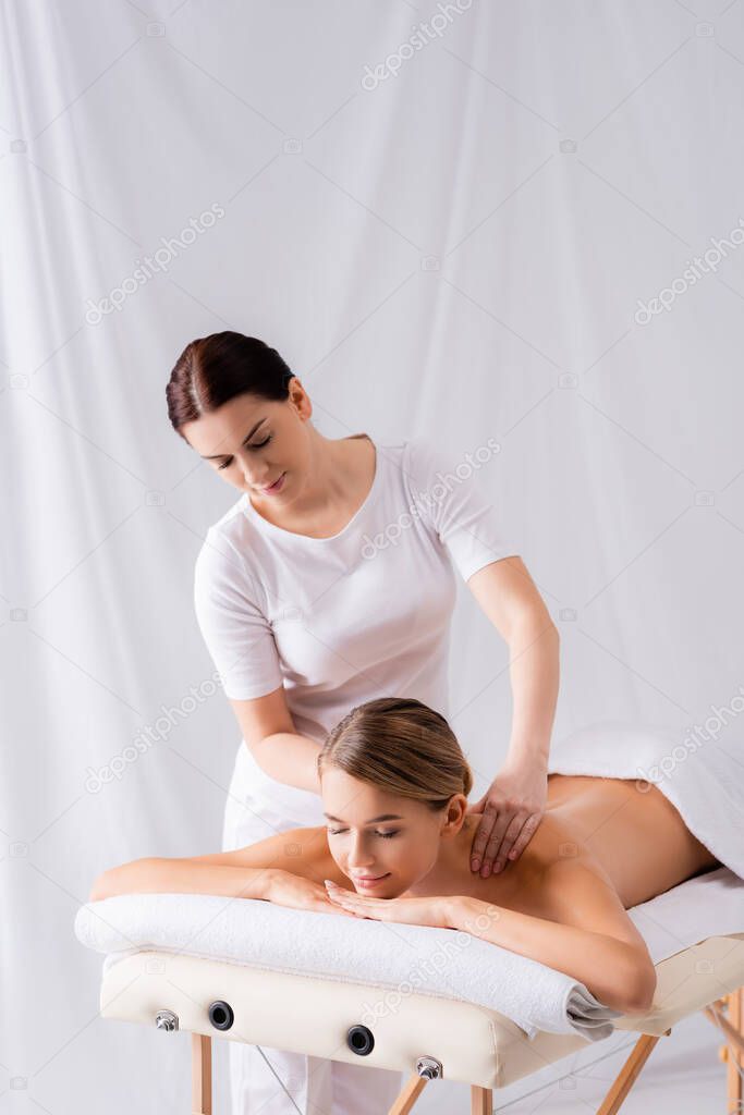 female masseur massaging pleased woman lying on massage table in spa salon