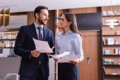 positive interracial business colleagues talking while holding papers in restaurant