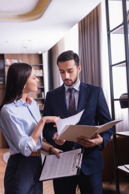 İş kadını sözleşmeyi tutuyor ve Müslüman iş ortağının yanındaki kağıtlara işaret ediyor.