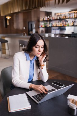 Lokantada dizüstü bilgisayarın ve akıllı telefonun yanında daktilo yazan konsantre serbest yazar.