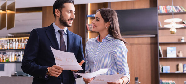 arabian businessman pointing at document near smiling businesswoman in restaurant, banner