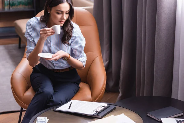 young businesswoman drinking coffee near contract in restaurant