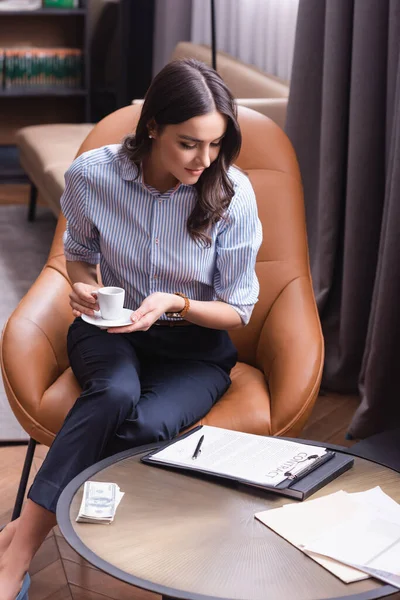 Affärskvinna Med Kopp Kaffe Sittande Fåtölj Nära Kontrakt Och Dollar — Stockfoto