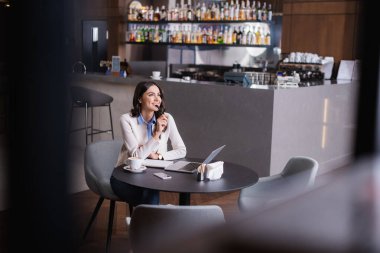 Lokantada dizüstü bilgisayarın yanında otururken gözlerini kaçıran mutlu, hayalperest serbest yazar.