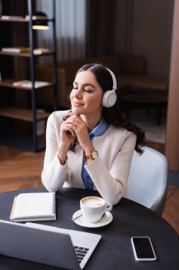 Gülümseyen, hayalperest, restoranda kablosuz kulaklıkla müzik dinleyen.