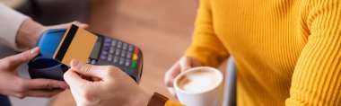 partial view of man holding cup of coffee and credit card near payment terminal in hands of waitress, blurred background, banner clipart