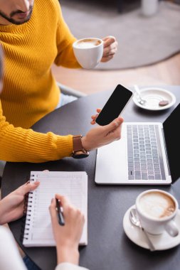 Kahve ve dizüstü bilgisayarın yanında arkadaşı olan arkadaşa ekranda akıllı telefonu gösteren kırpılmış görüntü 
