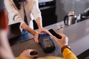 Lokantadaki ödeme terminalinin yakınındaki akıllı telefondan ödeme yapan adamın görüntüsü. 