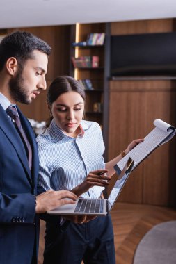 Restoranda panosu olan iş arkadaşının yanında dizüstü bilgisayar kullanan Arap işadamı. 