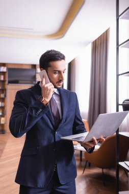 Müslüman işadamı akıllı telefondan konuşuyor ve restoranda dizüstü bilgisayar kullanıyor. 