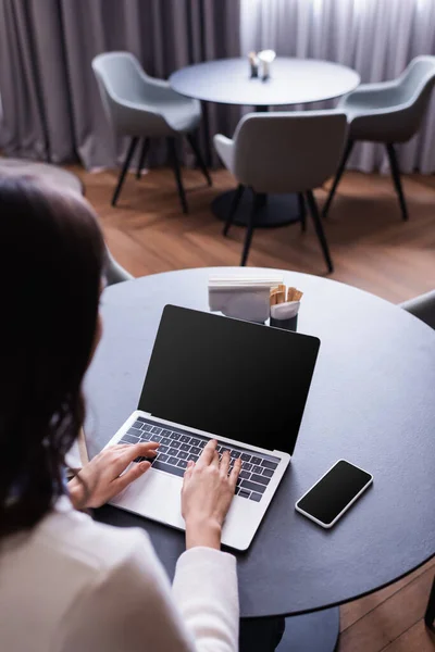咖啡店内带有空白屏幕的笔记本电脑上远程工作人员打字的高视角 前景暗淡 — 图库照片
