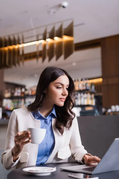 Koncentrerad Frilansare Hålla Kopp Kaffe Samtidigt Skriva Laptop Restaurang Suddig — Stockfoto