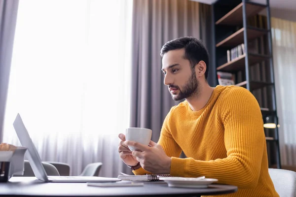 Concentrated Arabian Freelancer Holding Cup Coffee While Looking Laptop Restaurant — Stock Photo, Image