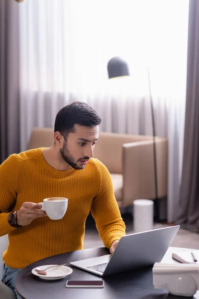 Surprised Arabian Freelancer Holding Cup Coffee While Looking Laptop Restaurant — Stock Photo, Image