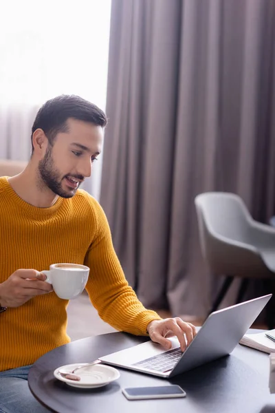 Smiling Arabian Freelancer Holding Cup Coffee While Typing Laptop Restaurant — Stock Photo, Image