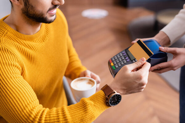 partial view of arabian man paying through payment terminal in hands of waitress