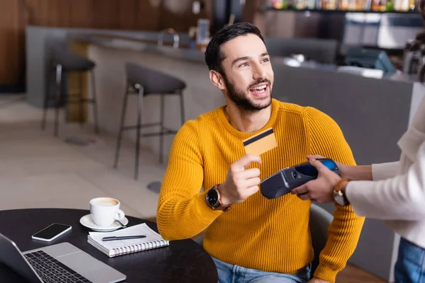 happy arabian freelancer holding credit card near payment terminal in restaurant