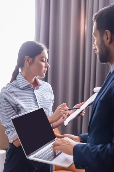 Geschäftsfrau Blickt Auf Klemmbrett Neben Arabischem Partner Mit Laptop Unscharfen — Stockfoto