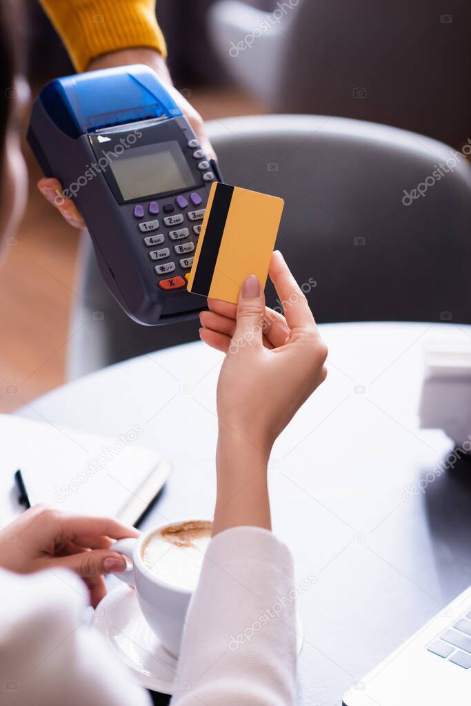 partial view of woman holding credit card near credit card reader in hand of waiter