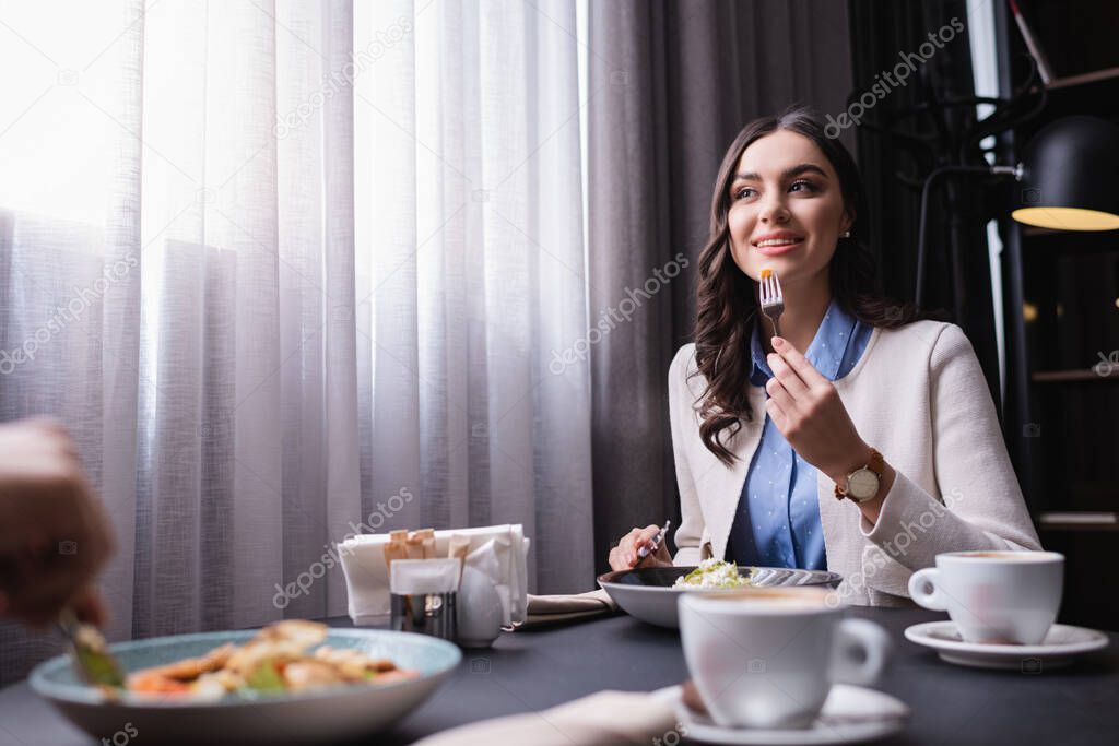 Smiling woman dinning with boyfriend on blurred foreground in restaurant 