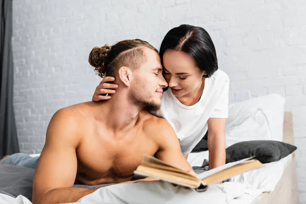 Young Woman Kissing Boyfriend Book Blurred Foreground Bedroom — Stock Photo, Image