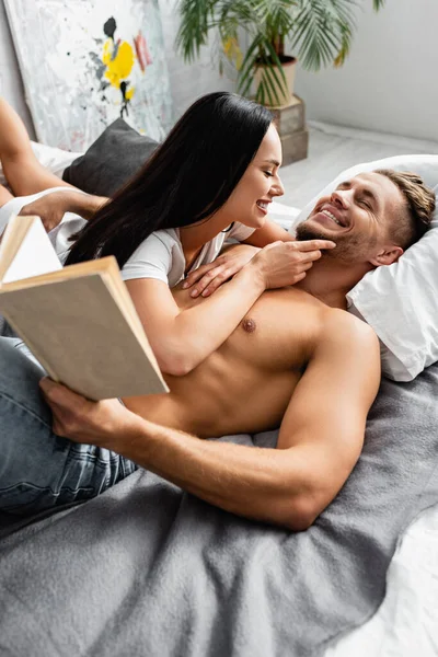 Mujer Alegre Tocando Barbilla Hombre Sexy Con Libro Cama — Foto de Stock