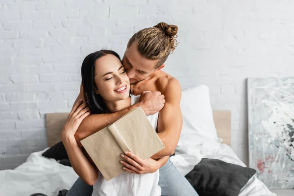 Hombre Sin Camisa Abrazando Mujer Alegre Con Libro Cama Casa — Foto de Stock