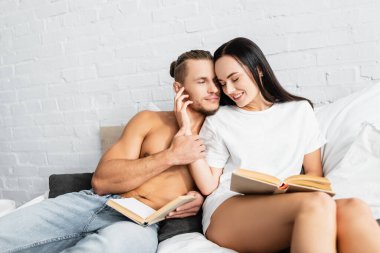 Kitabı olan gülümseyen kadın, kaslı adamın yanında oturuyor. 