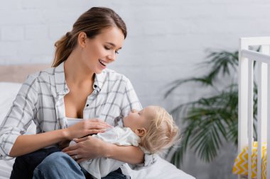 Mutlu genç anne, yatak odasında otururken bebeğini sakinleştiriyor.