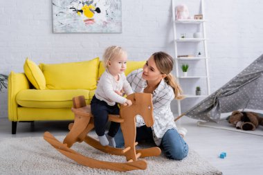 Güler yüzlü anne evde sallanan ata binerek güneşi destekliyor.