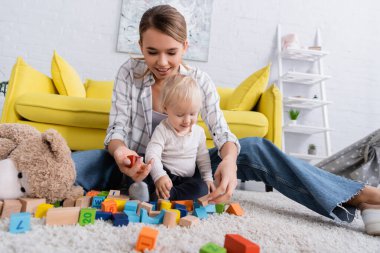 Mutlu anne küplerle oynuyor. Halıdaki çocukla birlikte. Ön plan bulanık.