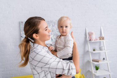 Mutlu genç bir kadın kucağında bebekle kameraya bakıyor. 