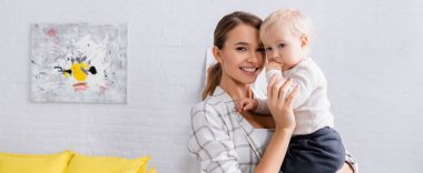 Genç bir kadın kameraya gülümserken kucağında oğlan, afiş