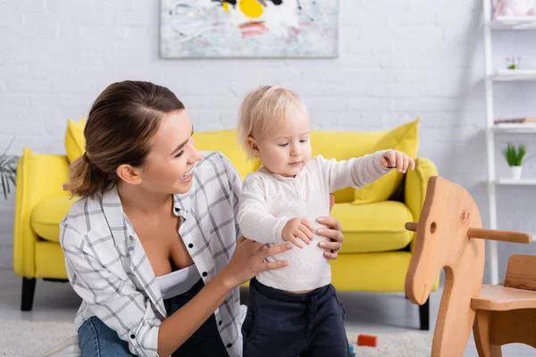 Laughing Woman Supporting Toddler Standing Rocking Horse — Stock Photo, Image