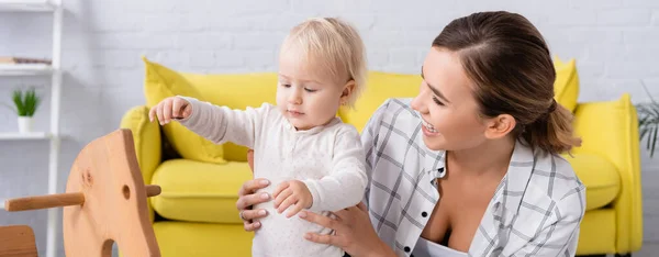 Junge Fröhliche Frau Unterstützt Kleinen Jungen Der Neben Schaukelpferd Steht — Stockfoto