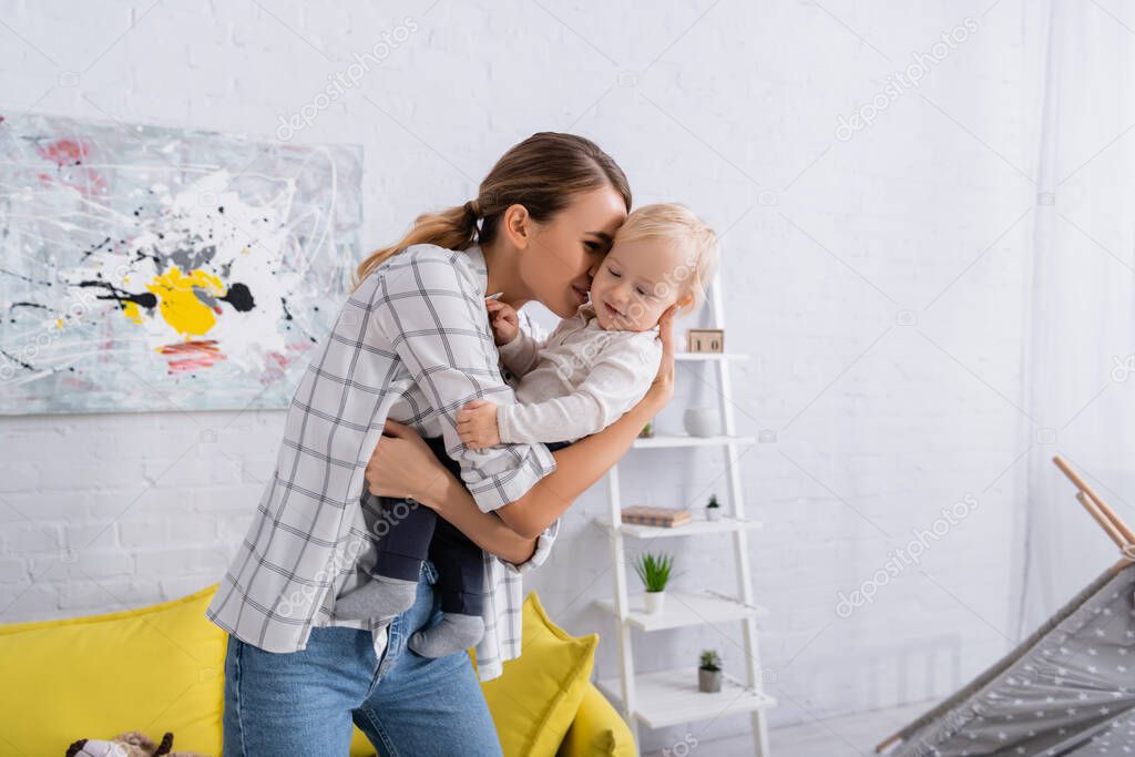 young woman holding and embracing toddler son at home