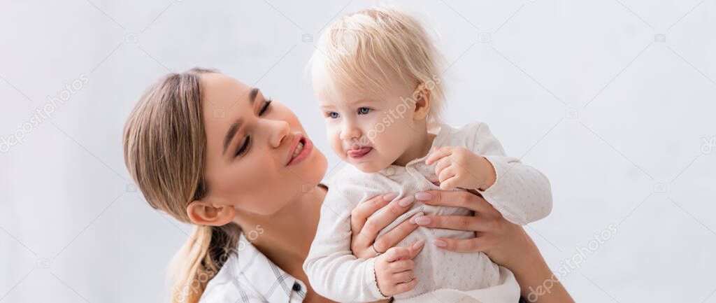 cheerful woman holding little boy sticking out tongue, banner