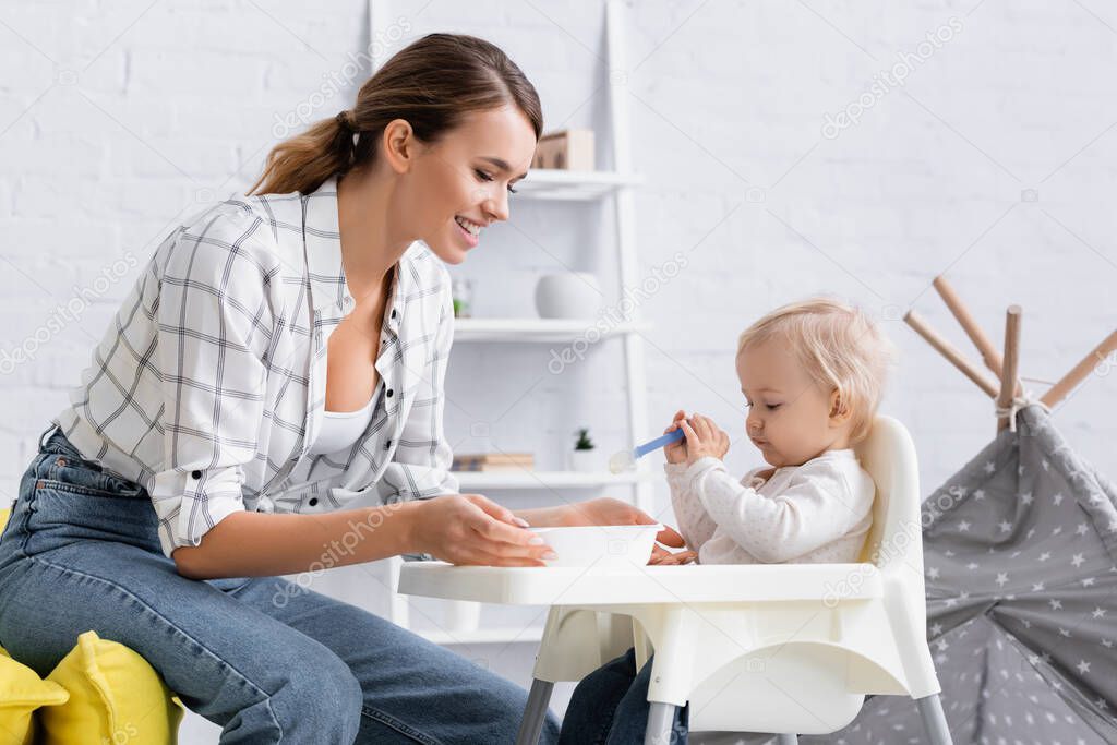 little boy sitting on kids chair with spoon near happy mother