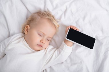 Beyaz ekranlı akıllı telefonun yanında uyuyan bebeğin üst görüntüsü.