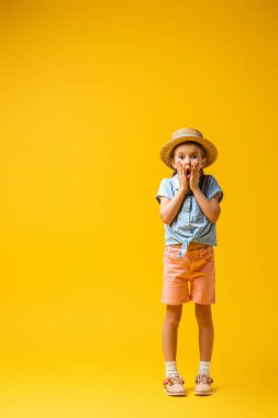 Hasır şapkalı bir çocuk sarı kameraya bakıyor.