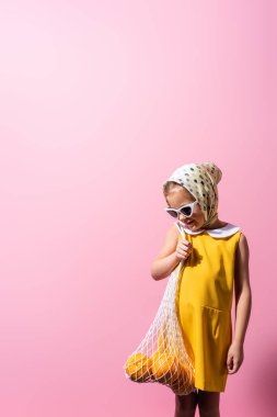Başörtüsü ve güneş gözlüğü takan mutlu bir kız. Elinde tekrar kullanılabilir pembe iplik torbası var.