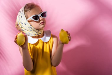 Türbanlı şık bir kız ve pembe üzerinde limon tutan güneş gözlüklü. 