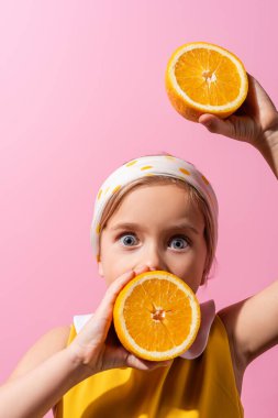 Şok olmuş, başörtüsü takmış ağzı turuncu yarı izole olmuş pembe elbiseli bir kız. 