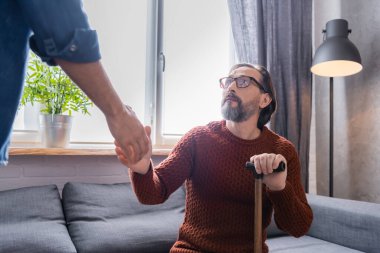 Elinde baston olan sakallı adam bulanık ön planda oğluyla el sıkışıyor.