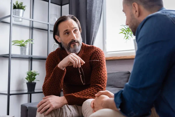 Gözlük tutan sakallı adam bulanık ön planda İspanyol oğlunu dinlerken