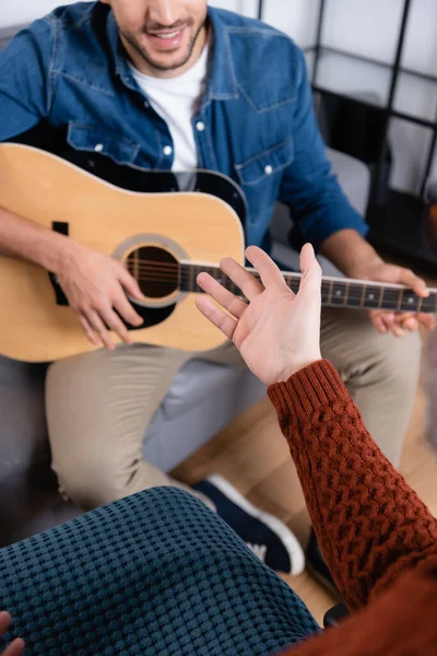 cropped view of handicapped man pointing with hand near son playing guitar on blurred background