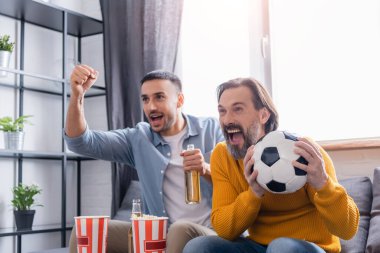 İspanyol oğlunun yanında bağıran heyecanlı adam evinde futbol maçı izlerken zafer işareti yapıyor.