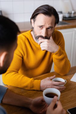 Mutfakta konuşurken oğlunu dinleyen düşünceli bir adam, ön planda bulanıklık...
