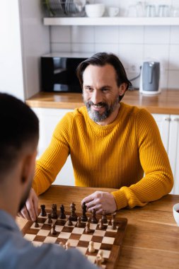 Mutfakta oğluyla satranç oynayan neşeli sakallı adam.